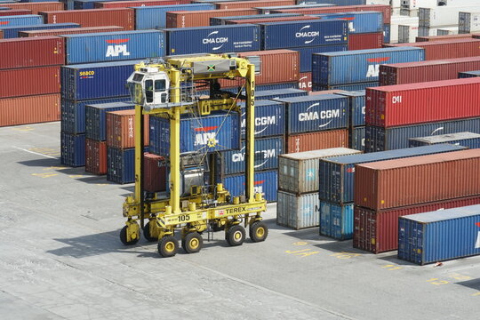 Kingston, Jamaica - 05 03 2023: A yellow empty straddle carrier without loaded container in Kingston Freeport Terminal passing near plenty of other boxes from various shippers.