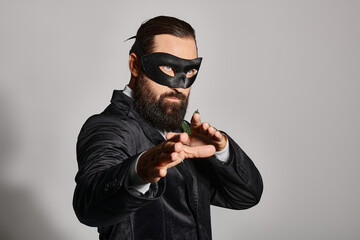 Christmas Masquerade ball, handsome bearded man in carnival mask and elegant suit on grey backdrop