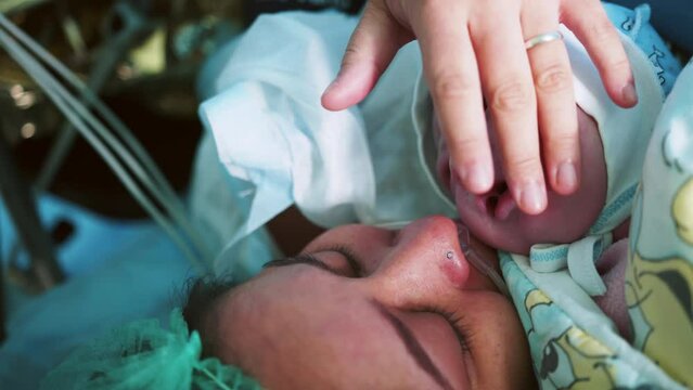 Mother Holds Newborn Baby in Hospital. Mother Holding Her Newborn Baby on Her Chest Just After Delivery. First Sight of Mom and Her Newborn in Operation Room. Modern Hospital Operation Room