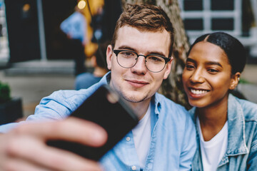 Cheerful diverse friends taking pictures on mobile phone resting outdoors