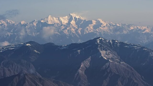 Time-lapse of the Himalayan snow-capped mountains during sunrise with moving clouds and blue sky in the background. The Himalayas as seen from Uttarkashi, Uttarakhand during the winter season.