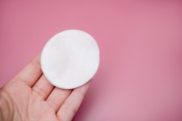 Girl holding clean cotton pad in her hand, sponge for removing make-up, on pink background