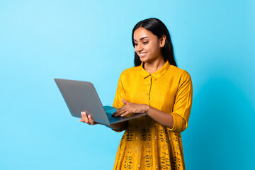 Happy young Hindu lady using her laptop computer, blue background