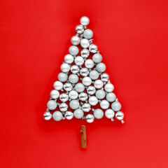 Creative Christmas concept. Silver Christmas tree balls laid out in the shape of a Christmas tree on a red background.