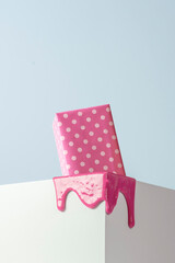 Creative gift concept. Gift box wrapped in pink polka dot gift paper melts on the end of a white cube.