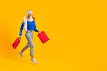 Joyful shopper with red bags during winter sale on yellow backdrop