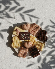small handmade pink, white, brown chocolates in a bowl on a white textured background with shadows from plants, holiday gift