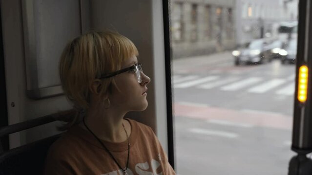 A girl sits and rides on a bus or tram, looking out the window. Cityscape, public transport.