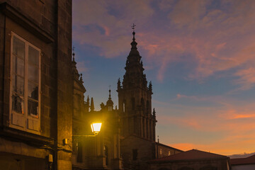 Obraz premium In the foreground, a lit lantern, in the background, stands one of the towers of the Cathedral of Santiago de Compostela, with a beautiful sunset sky in the background