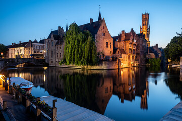 Famous medieval buildings of Brugge with beautiful reflection illuminated during blue hour  - obrazy, fototapety, plakaty