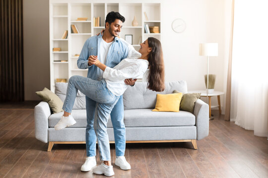 Playful Indian couple dancing in a well-lit, modern living room