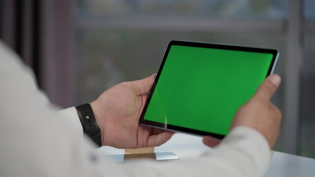 Close up of Tablet Computer with Green Screen Mock Up Display In Men's Hands. Man Watching Videos and Reading Social Media Posts on Mobile Device