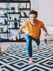 Motivated hipster guy warming up before meditation in modern apartment