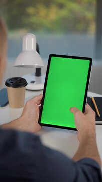Young Man Using Tablet Computer with Green Screen Mock Up Display. Male Watching Videos and Reading Social Media Posts on Mobile Device. Shooting Close Up Over the Shoulder