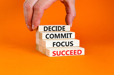 Decide commit focus succeed symbol. Concept word Decide Commit Focus Succeed on wooden block. Beautiful orange background. Businessman hand. Business decide commit focus succeed concept. Copy space.