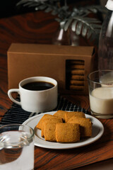 Crunchy cookies biscuits served in plate with cookie box, black coffee and glass of milk isolated on table side view of american cafe baked food