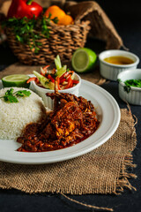 Jamaican Mutton gravy with plain rice, salad, tomato, cucumber dip, sauce and bell pepper served in plate isolated on napkin side view of lunch food