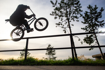 Urban biker performing acrobatic jump at sunny sky - Guy riding bmx bicycle at extreme sport...