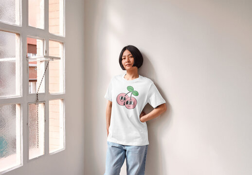 Mockup of young Asian woman wearing customizable t-shirt leaning on wall