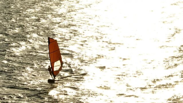 silhouette of a person windsurfing in the ocean. Active extreme beach vacation on a board in the sea. High quality 4k footage
