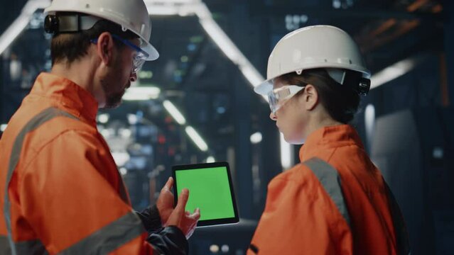 Engineer teaching woman intern on factory showing green screen tablet close up.