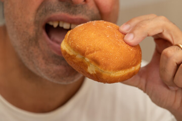 man eating Bola de Berlim or Berlim Ball, a Portuguese pastry made from a fried donut filled with sweet cream