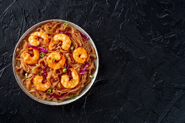 Konjac pasta. Shirataki fettuccine with shrimps and vegetables, a healthy diet dish, overhead flat lay shot on a black background with copy space
