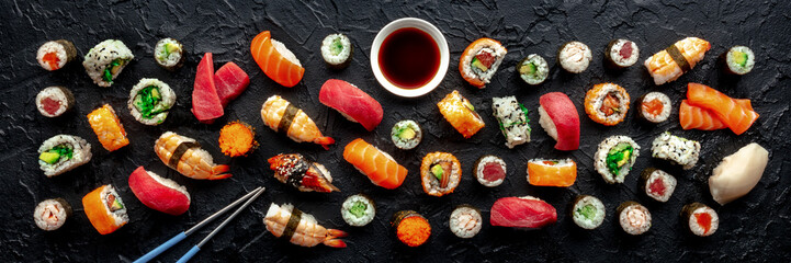 Sushi with chopsticks and soy sauce panorama. Many rolls, maki, nigiri etc, overhead flat lay composition on a black background. Japanese restaurant