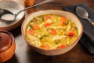 Chicken noodle soup with vegetables, a bowl of healthy broth with a ladle, on a rustic wooden table, winter comfort food