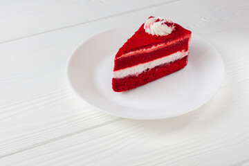 A mouthwatering slice of red velvet cake with creamy white frosting, presented on a wooden table. A...