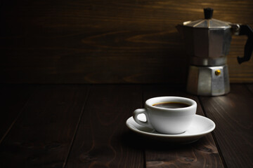 Cup of coffee with metal coffee percolator on dark wooden background
