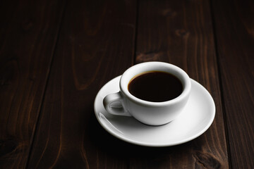 Close up white coffee cupon black wood table with light shade on tabletop at cafe.