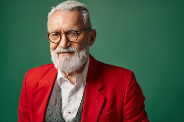 jolly Santa Claus with beard and glasses posing on green backdrop looking at camera, winter concept