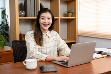 Happy Asian girl in office with laptop looking at camera Smiling Asian student using computer at office Successful stylish businesswoman