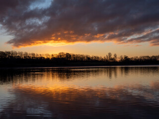 Winter sunrise over water.  The December sun peeks above the horizon and sends golden rays out across the water in Warwickshire, England