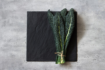 Bunch of black tuscan kale (cavolo nero or lachinato kale) on a black slate board on a gray textured background, top view