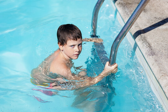 Boy in a pool gripping ladder with intent gaze.