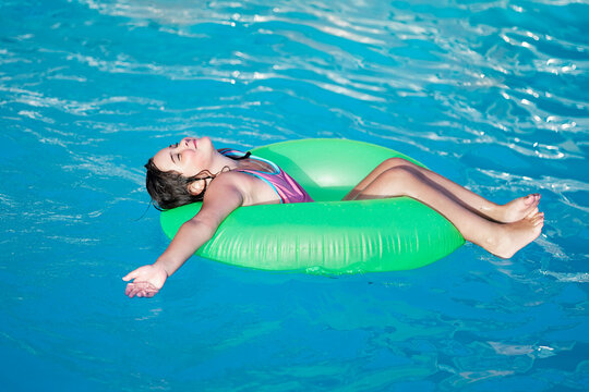 Girl on green float enjoying serene pool moment.