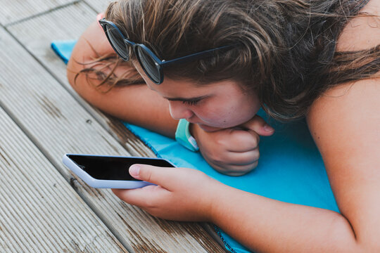 Girl lying on a blue towel using a smartphone.