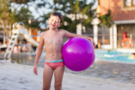 Boy with purple beach ball by poolside.