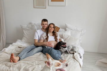 Couple in love, pregnant girl and guy with dogs on bed, bright photo