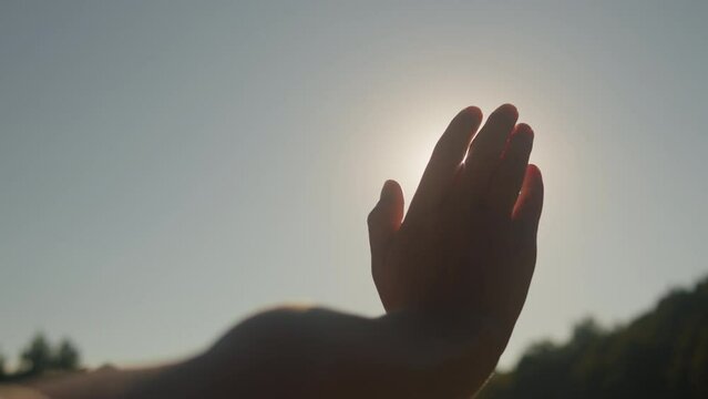 Hand of young woman at sunset close-up. Sun between the hands of tourist girl. Silhouette of happy dreaming female pulls her hand to the sun. Calm meditation