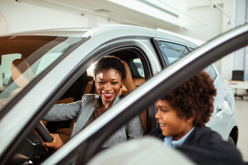 Joyful mother and son exploring a new car at a dealership