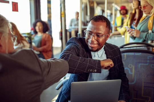 Businessman using an elbow bump to greet a friend while commuting to work on a bus