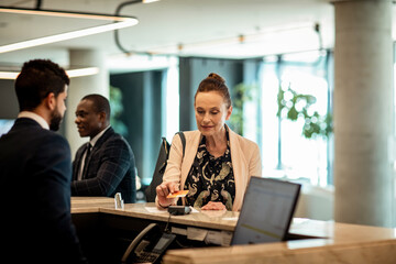 Middle aged woman paying the hotel stay with her credit card at the reception