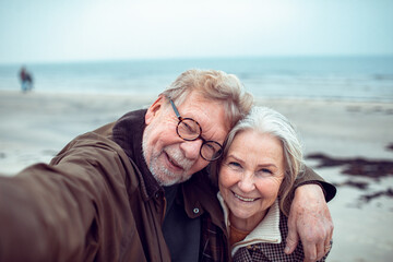 Happy senior couple taking a selfie at the beach during winter