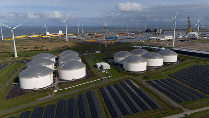 Solar panel park with windmills and fuel silos and harbor in background, Aerial