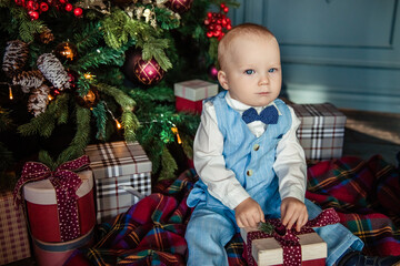 Cute kid in blue suit sitting under Christmas tree with gifts