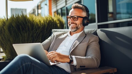 Balancing work and relaxation: A middle-aged businessman enjoys music and productivity while working remotely with headphones - obrazy, fototapety, plakaty