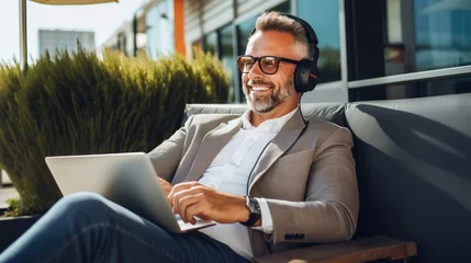 Foto op Plexiglas Balancing work and relaxation: A middle-aged businessman enjoys music and productivity while working remotely with headphones © pvl0707